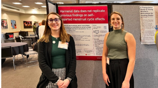 Two individuals stand near a research poster in a conference room.